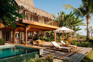 a villa with a pool and a deck with chairs and an umbrella at NIHI Sumba - 50 Best Hotels of the World in Watukarere