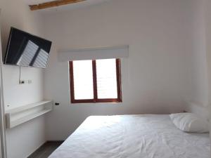 a white bedroom with a bed and a television at Casa los Pinos in Zorritos