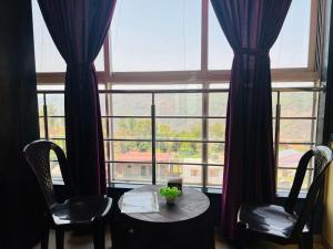 a room with a table and two chairs and a large window at Hotel Nisha in Mahabaleshwar