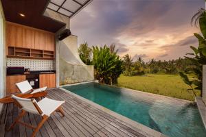 a pool with two chairs and a table on a deck at Subu Utamas Villas in Ubud