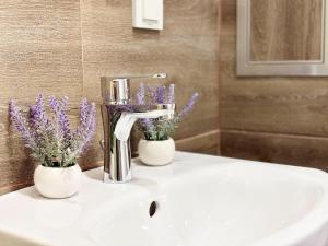 a bathroom sink with two white vases with purple flowers at Modern Nest Varna - free parking in Varna City +17 photos