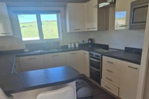 a kitchen with white cabinets and black counter tops at 2 Bed Caravan - Sleeps 6 - Pets - Pool - Parking in Newquay