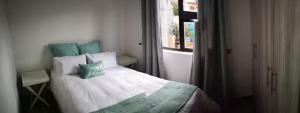 a bedroom with a bed with green pillows and a window at Memoirs in Cape Town in Zeekoevlei