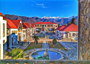 a building with red roofs and a fountain with mountains in the background at Garden Sheki Hotel in Sheki