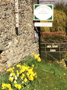a sign in front of a stone wall with yellow flowers at High Wray Farm in Ambleside