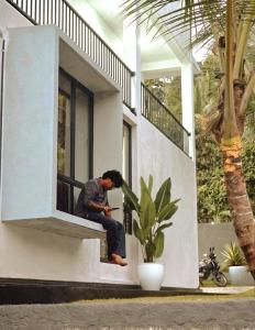 a man sitting on a window sill looking at his cell phone at The Paddy Breeze Villa in Marukwatura