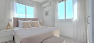a white bedroom with a bed with a chair and windows at White Aura by Staycom in Paphos
