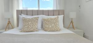 a bed with white pillows and a large window at White Aura by Staycom in Paphos