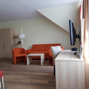 a living room with an orange couch and a tv at Hotel am Stadtpark in Hilden