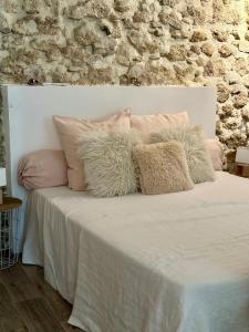 a white bed with pink pillows and a stone wall at Domaine La Parpaille in Cucuron