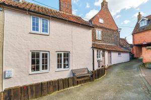 a white building with a bench next to a street at Channel Cottage in Wells next the Sea