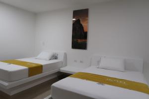 two beds in a white room with a picture on the wall at Hotel Puerto Triunfo in Doradal