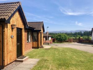 a wooden house with a door and a grass yard at Manuka Cottage in Aviemore