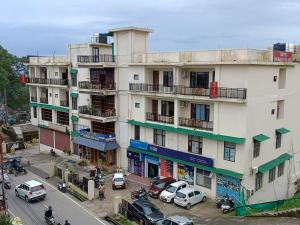 a tall white building with cars parked in front of it at Hotel Dewan Palace in Dharmsāla