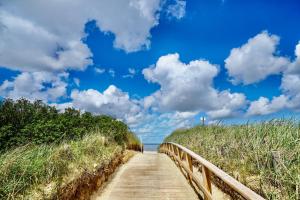 a wooden path to the beach with a blue sky and clouds at Seehütte 004 in Cuxhaven