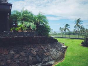 a stone retaining wall in front of a yard with palm trees at Unit 25 Hula Hut Best Value in Pahala