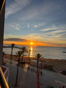 a sunset on a beach with palm trees and the ocean at LUSAIL 1ª línea playa ADULTS ONLY in Vinarós