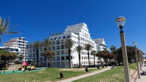 a large white building with palm trees in a park at Apartamento Kélyfos Beach by feriascomsol in Quarteira