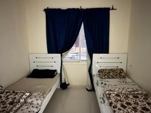 two beds in a room with a window with blue curtains at Stay home in ‘Uqayr