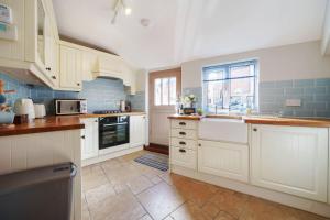 a kitchen with white cabinets and blue tiles at Channel Cottage in Wells next the Sea