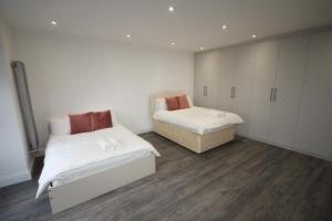 two beds in a room with white cabinets and wood floors at Osterley Place - Apt A in Hounslow