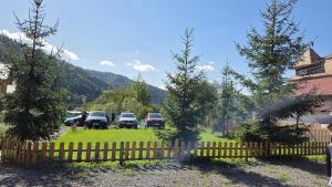 a fence with cars parked in a yard with trees at Cabana Mareea -Lunca Bradului in Lunca Bradului