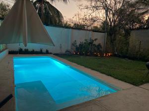 a blue swimming pool in a yard with a umbrella at Jungle surf Villa in El Zonte +10 photos