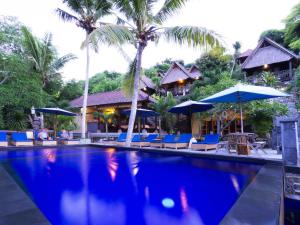 a pool at a resort with chairs and umbrellas at Song Lambung Beach Huts in Nusa Lembongan