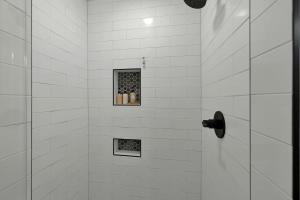 a white tiled shower with a shelf with bottles at Rojo-Charming unit walking distance to Main St! in Fredericksburg +6 photos