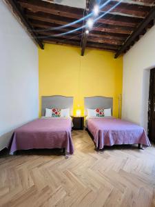 two beds in a room with yellow walls and wooden floors at Casa Universidad in Guanajuato