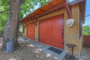 a garage with a red door next to a tree at Tejas Suite Walking Distance to Main St! in Fredericksburg
