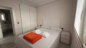 a white bed with an orange towel on it at Turquesa 10 in La Pineda