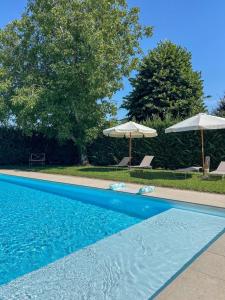 a blue swimming pool with umbrellas and chairs and trees at b&b VillaGresana in Villafranca di Verona