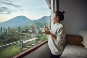 a woman holding a cup of coffee looking out a window at Pondok Alengkong in Bangli +60 photos