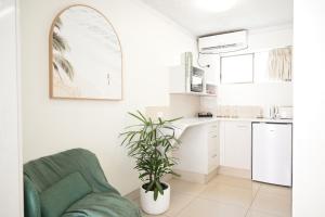 a white kitchen with a green chair and a plant at Bay Motel in Byron Bay