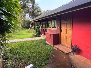 a red house with a wooden door and a yard at My Mountain Home - Le Chalet in Afaahiti