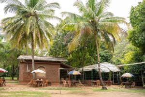 two palm trees and a building with tables and umbrellas at Sayon River Cottage in Wellawaya +13 photos