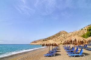 a row of chairs and straw umbrellas on a beach at Myrtos Mare Suites in Myrtos