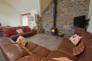 a living room with leather couches and a stone wall at Deri Lleyn in Sarn