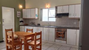 a kitchen with white cabinets and a wooden table and chairs at Anchorage in Stompneusbaai
