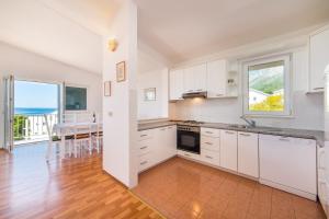 a kitchen with white cabinets and a dining room with a table at Apartmani More in Gradac