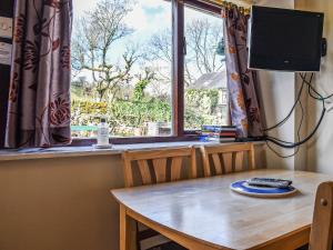a dining room table with a television and a window at Stable Cottage in Leek