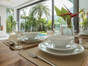 a wooden table with plates and glasses on it at Calypso Villa Phuket - Naiyang Beach in Nai Yang Beach
