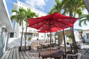 a red umbrella on a wooden deck with tables and chairs at Hanamuro Inn Aka Island in Zamami