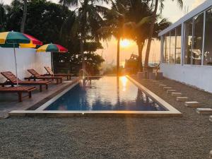 a swimming pool with benches and umbrellas in front of a building at Danish Crown Hotel in Ambalangoda