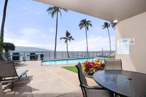 a patio with a table and chairs and a pool at Lauloa 105 · LOA 105 2BD OceanFront Getaway w AC Pool in Wailuku