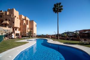 a swimming pool with a palm tree and buildings at Seaview Apartment - COTO REAL Duquesa in Manilva
