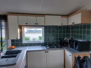 a kitchen with white cabinets and a sink and a window at JOY Boutique Chalet Berkhout - Hoorn in De Hulk +37 photos