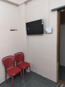two red chairs in a room with a tv on a wall at Swarna Lodge in Badami