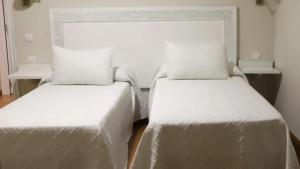 two beds in a room with white sheets and pillows at Hotel Recio in Santa Olalla de Toledo